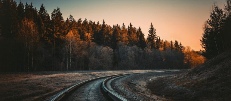 A serene view of a railway track in a forest at sunset with Autumn colors.